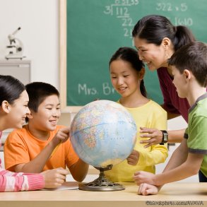 Teacher and students viewing globe in geography classroom